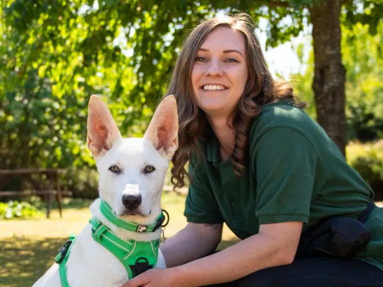 Jo the intake and assessment officer smiling while holding white dog in the countryside