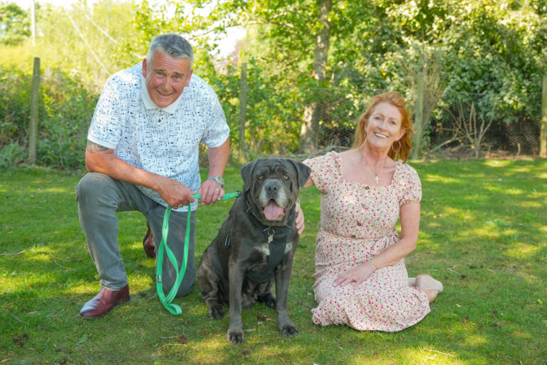 A couple kneel on a grass lawn with their large dog.